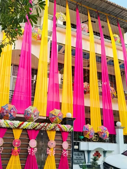 I can transform the entire look of your home for a wedding celebration. Here, I used long drapes of bright pink and yellow fabric to cover the building's facade, creating a festive 'ghar ki shaadi' look that's visible from the street.