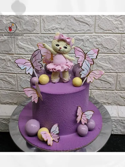 A whimsical ballet-themed cake featuring a teddy bear ballerina surrounded by delicate butterflies. The rich purple frosting and pastel details make this a magical choice for a birthday celebration.