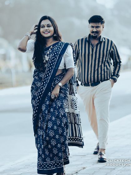 A candid walking shot of a couple in traditional attire, with the bride in focus, set against a blurred city street.