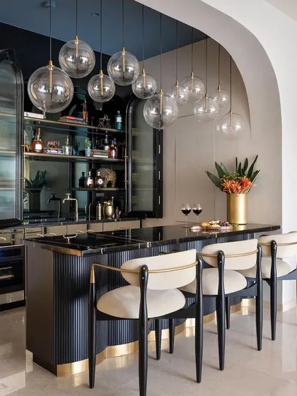 A stunning home bar from the Studio Sylus project, featuring our custom bar stools. The stools have a black wood frame, cream upholstery, and a gold-finished metal accent, perfectly complementing the bar's design.