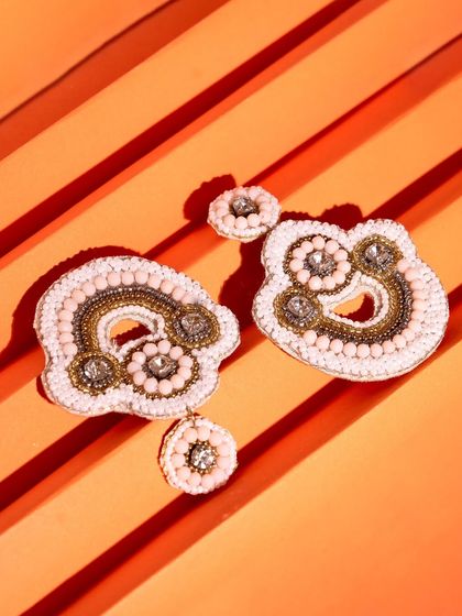 Beaded statement earrings arranged on a vibrant, striped orange background. This top-down shot is bold and perfect for social media.