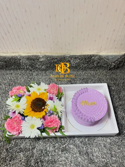 A lovely Mother's Day tray with a purple "Mom" cake and a bright arrangement of sunflowers and carnations.