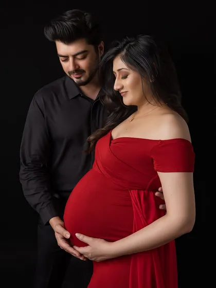 A classic couple's portrait against a dramatic black background. The focus is entirely on their expressions and the baby bump.