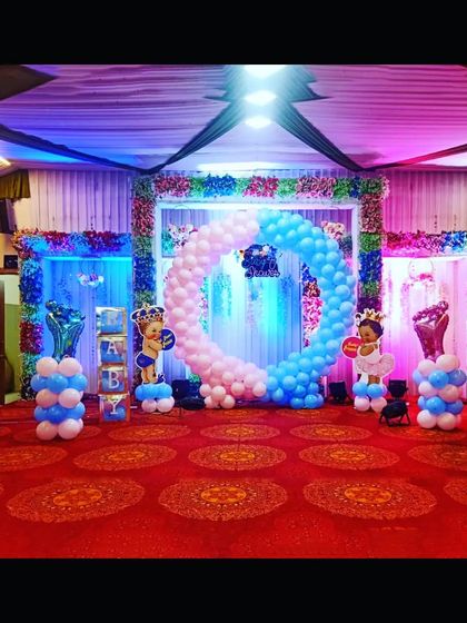 A wide view of the gender-reveal baby shower setup, showing the full stage with balloon columns and a vibrant red carpet.