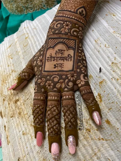 Traditional blessings can be a beautiful part of your henna. This design features the auspicious Sanskrit phrase 'Sada Saubhagyavati Bhava' as the central element on the back of the hand.