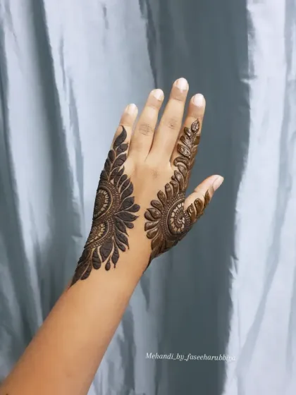 The completed bold henna design, featuring a large, leafy pattern that extends up the side of the hand.