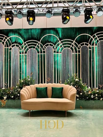 A glamorous reception stage with an art deco feel, using green velvet drapes, white arched frames, and string details for a sophisticated look.