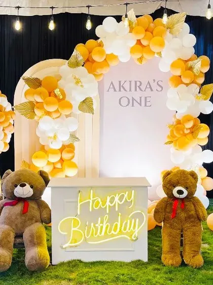 A closer look at the outdoor teddy bear setup, highlighting the clean arched backdrop and the warm glow of the neon sign against the evening sky.