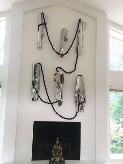 The full view of the early installation above a fireplace, exploring space and emotion with stainless steel forms connected by a thick black rope.