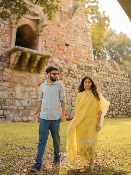 A couple enjoys a walk through a historic park, their traditional yellow outfits glowing in the soft light.