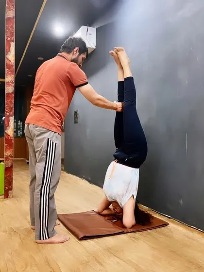 My hands guide the student's legs in this wall-assisted headstand, helping her find the feeling of stacking her hips over her shoulders.