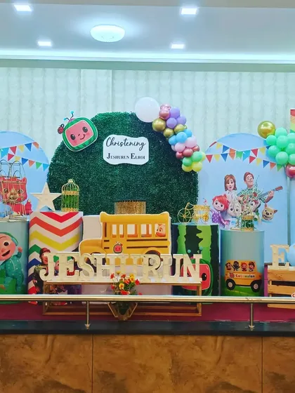 This colorful Cocomelon themed setup was for a Christening ceremony. It features character cutouts, a custom school bus prop, and a faux grass backdrop, combining a fun kids' theme with a traditional event.