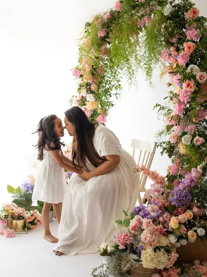 A tender nose-to-nose kiss between a mother and daughter, surrounded by a beautiful arch of flowers from a Mother's Day mini session.