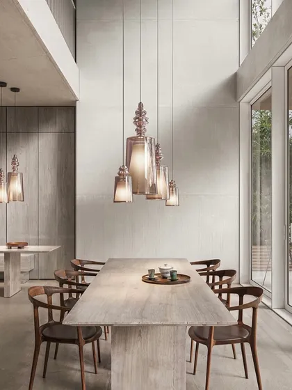 A cluster of the iconic pendants creates a dramatic chandelier over a large dining table in a double-height space. The warm amber glass complements the natural wood and stone materials.