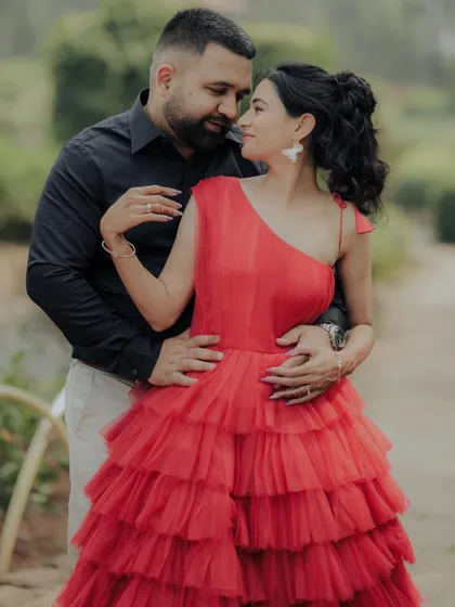 A close-up portrait capturing the couple's loving embrace. The focus is on their expressions and the intricate details of the bride-to-be's gown, set against the soft greenery of a park.