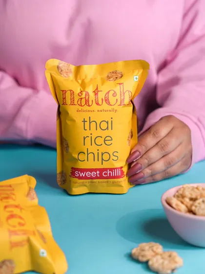 A lifestyle product shot for a snack brand, featuring a model holding the package. This style helps customers visualize the product as part of their daily routine, making it more relatable.