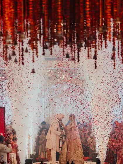 A shower of rose petals rains down on the couple during their varmala exchange. This iconic moment is amplified by dramatic lighting and a backdrop of hanging temple bells, creating a truly divine atmosphere.