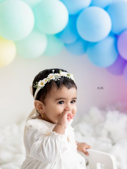 A sweet baby girl enjoying her first birthday shoot with a rainbow balloon backdrop.