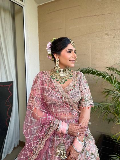 A smiling bride with her hair in a classic bun, adorned with a mix of pastel pink and green flowers to complement her ornate lehenga.