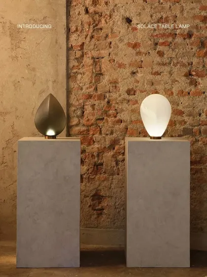 The two Solace table lamps are presented against a rustic brick wall, their modern, sculptural forms creating a striking contrast with the raw texture of the background.