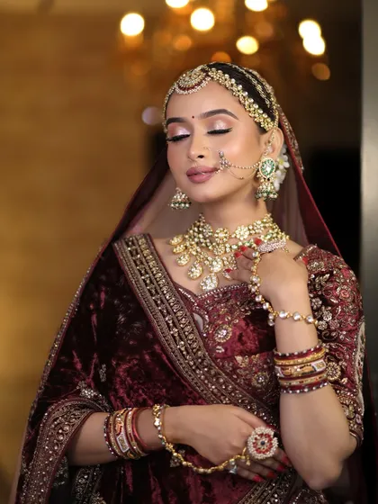 A close-up of a bride in a deep maroon velvet lehenga, adorned with a heavy Polki and Kundan set. The hathphool and nath are beautifully detailed, adding to the royal aesthetic.