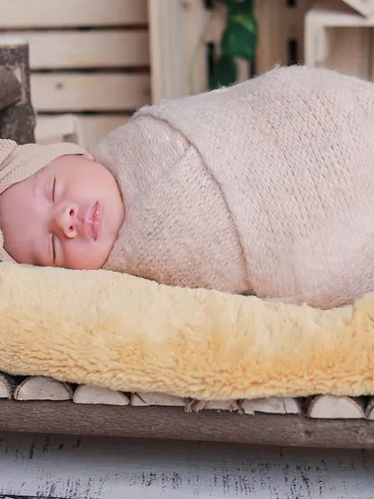 A close-up of the baby sleeping on the rustic log bed, wrapped in a neutral-toned swaddle. The textures of the wood and soft bedding create a lovely contrast.