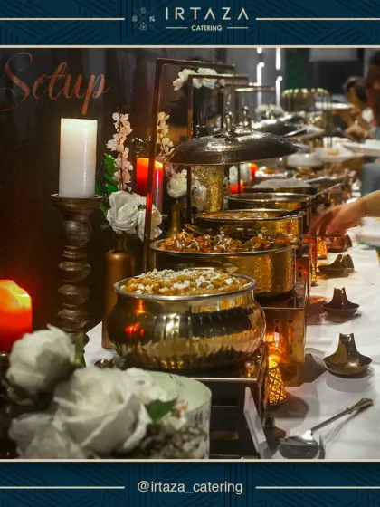 Guests helping themselves to a lavish spread served in gleaming golden pots. The scene is illuminated by tall candles and accented with white roses, capturing the warm and celebratory atmosphere of a well-catered event.
