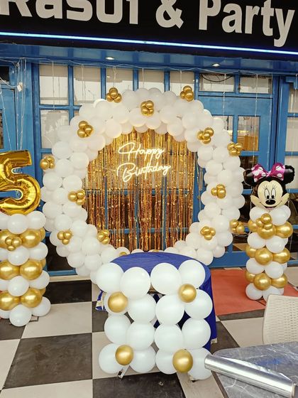 A Minnie Mouse-themed 5th birthday party with a white and gold color scheme. This setup includes a ring arch, light-up number, and a Minnie Mouse balloon pillar.
