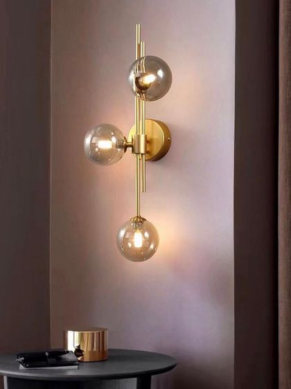 A modern wall sconce with three smoked glass globes on a brass fixture. This design is perfect for a hallway or living room.