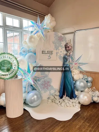 This wintery Frozen setup uses a white backdrop with snowflake details and iridescent starburst balloons. The "snow" on the floor and Elsa cutout create a magical, frosty scene.