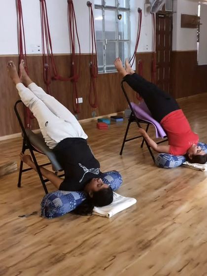 Two students in supported shoulderstand, showcasing how props can be adapted for different body types to achieve the same peaceful and restorative benefits.