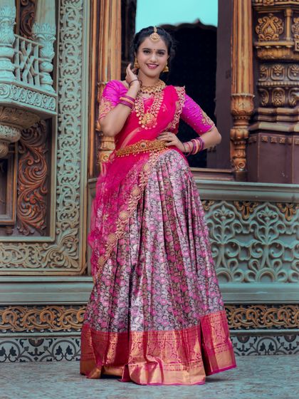 A full-length shot showcasing a half-saree bridal look. The combination of a bright pink top and a floral patterned skirt is modern yet traditional, and the makeup is designed to match this vibrant energy.