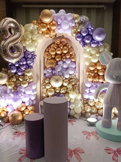 An elegant 8th birthday celebration with a teddy bear theme. The decor features a sophisticated balloon arch in purple, gold, and cream, a large number '8' foil balloon, and a stylized bear figure, showing how a kids' theme can be done with a touch of glamour.