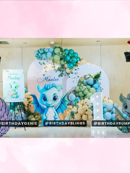 A unique and adorable baby dragon theme for a first birthday. The setup includes a large dragon egg prop, cute dragon cutouts, and a balloon arch in shades of green and cream.