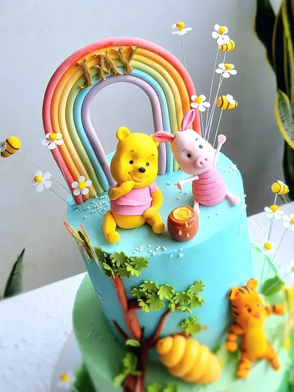 A close-up of the Winnie the Pooh and Piglet toppers under a pastel rainbow.