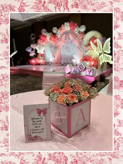 A beautiful table centerpiece from a pink Dior-inspired shower. A custom 'A' block holds a bouquet of pink and peach roses, next to a sweet welcome card for the baby.