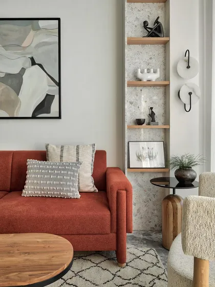 A close-up of the living area in Apartment 1101. The rust-colored sofa is paired with terrazzo shelves adorned with vibrant artifacts, exuding charm and personality.