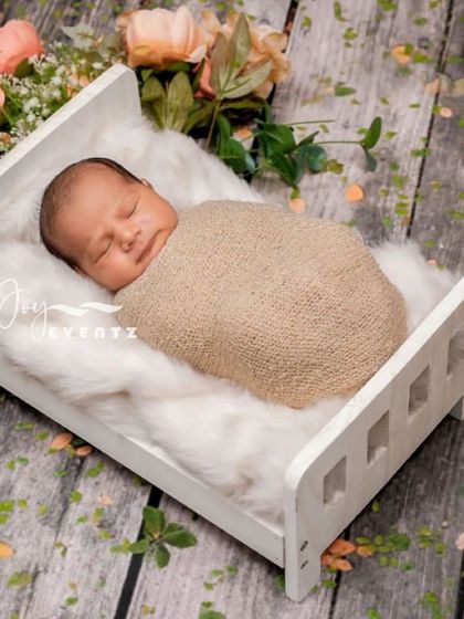 A classic and timeless newborn portrait featuring a baby sleeping on a miniature white wooden bed. The setup uses a soft fur blanket and a rustic wood floor backdrop for a cozy and serene feel.