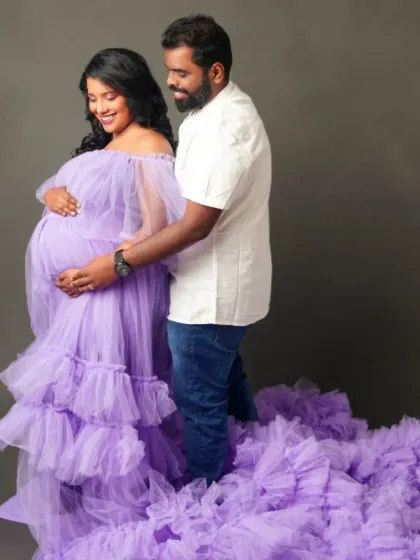 A tender moment captured in a sea of lavender tulle. This off-the-shoulder gown with its voluminous ruffled train is perfect for romantic couple's maternity portraits.