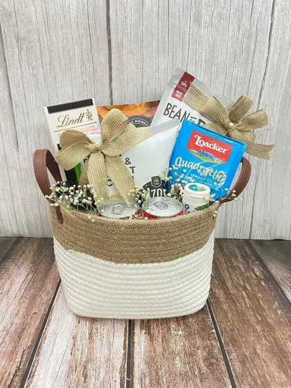A classic welcome hamper in a jute and cotton basket, filled with snacks and drinks, perfect for any occasion.
