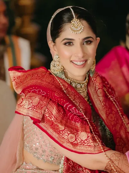 A happy bride on her Phera day, wearing a pastel pink lehenga and a traditional red bandhani dupatta.