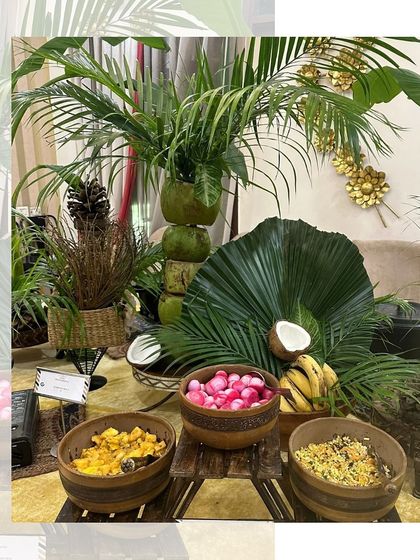 A tropical-themed setup for a Teej or Rakhi celebration. The decor features fresh coconuts, bananas, and palm leaves, creating a unique and refreshing vibe.