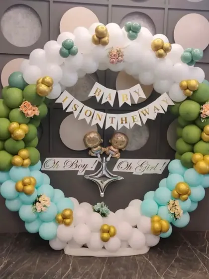 A gender-neutral "Baby Is On The Way" decoration. This circular balloon arrangement uses a refreshing color scheme of green, aqua, and white with gold accents, perfect for any baby shower.