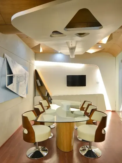 The conference room in my studio features a fluid, inclined partition clad in veneer that seamlessly continues onto the ceiling. A sliding glass wall allows the space to be either private or open, offering functional flexibility.