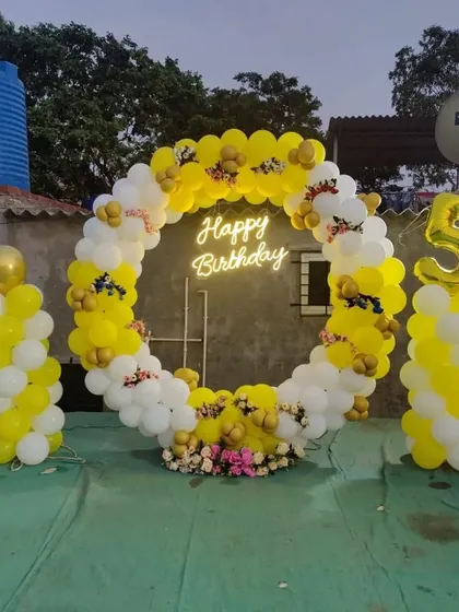A cheerful yellow and white balloon ring for a 5th birthday, set up on a rooftop and decorated with small flowers.