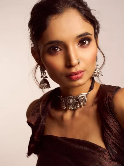 A modern take on traditional styling. This look pairs a contemporary brown outfit with classic silver jewelry, complemented by a soft smokey eye and a braided updo.