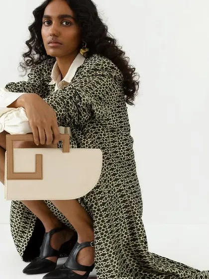 A full-length crouched pose, showing the complete outfit and how the handbag complements it. The composition is dynamic and modern.