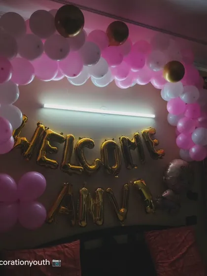 A sweet "Welcome Anvi" decoration. This bedroom setup features a pink and white balloon arch over the bed with the name in gold foil letters.