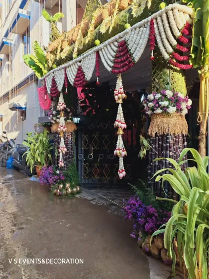 An angled view of the traditional house entrance, showing the intricate details of the hanging floral arrangements and the woven pillars.