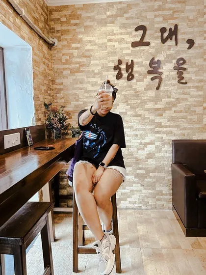 A fun, 'no-face' shot at a Korean cafe in Kolkata, holding up a drink. The Korean text on the wall adds to the authentic atmosphere.